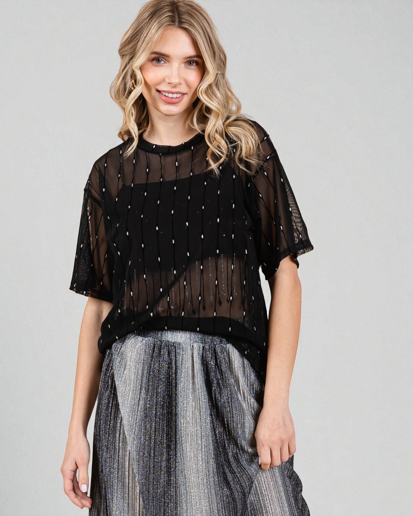 Woman wearing a black sheer top with embellishments and a gray skirt on a gray background