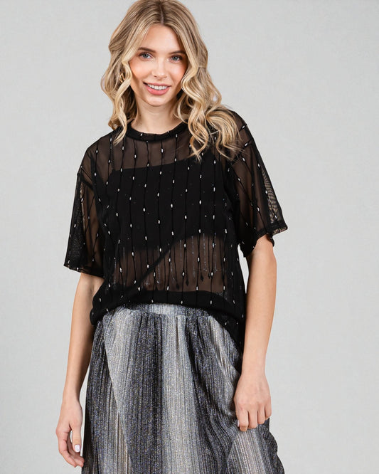 Woman wearing a black sheer top with embellishments and a gray skirt on a gray background