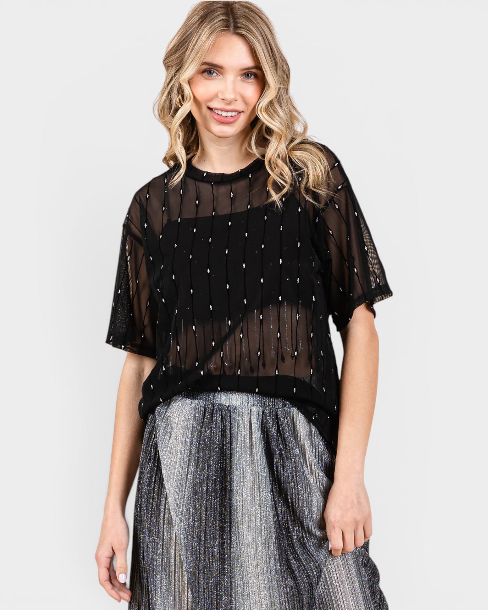 Woman wearing a black sheer top with silver embellishments and a gray skirt on a white background