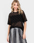 Woman wearing a black sheer top with silver embellishments and a gray skirt on a white background