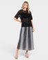 Woman wearing a black top with embellishments and a silver skirt on a white background