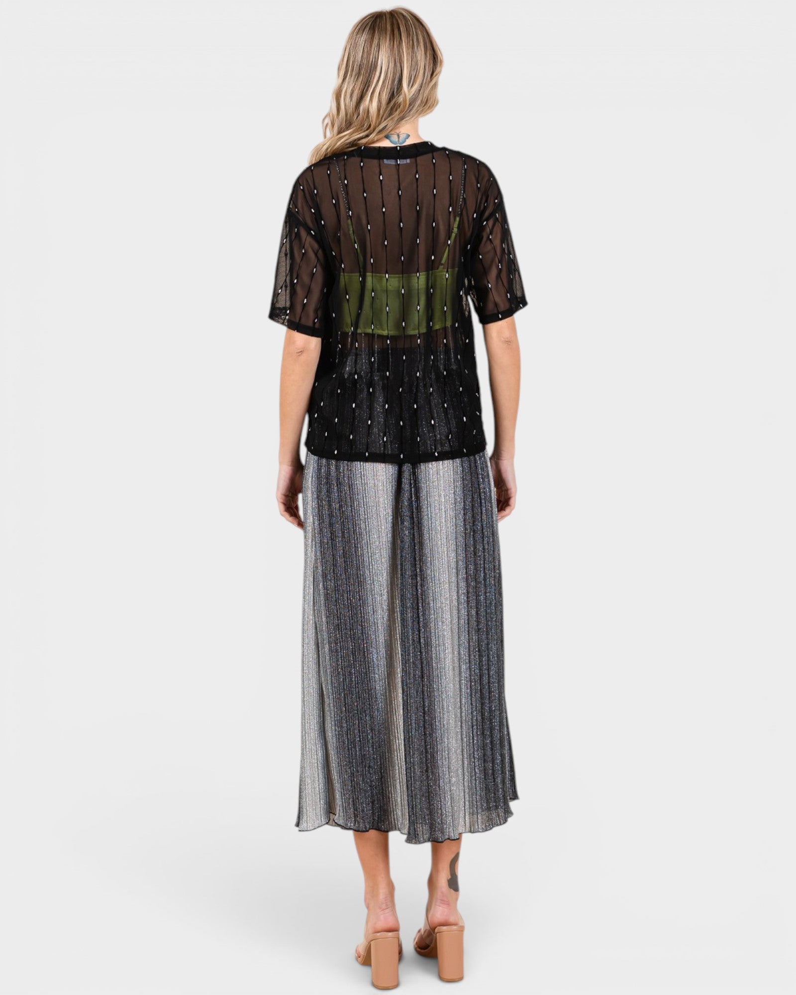 Woman wearing a black top with sheer sleeves and a long silver skirt on a white background