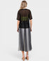 Woman wearing a black top with sheer sleeves and a long silver skirt on a white background