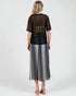 Woman wearing a black top with sheer sleeves and a long silver skirt on a white background