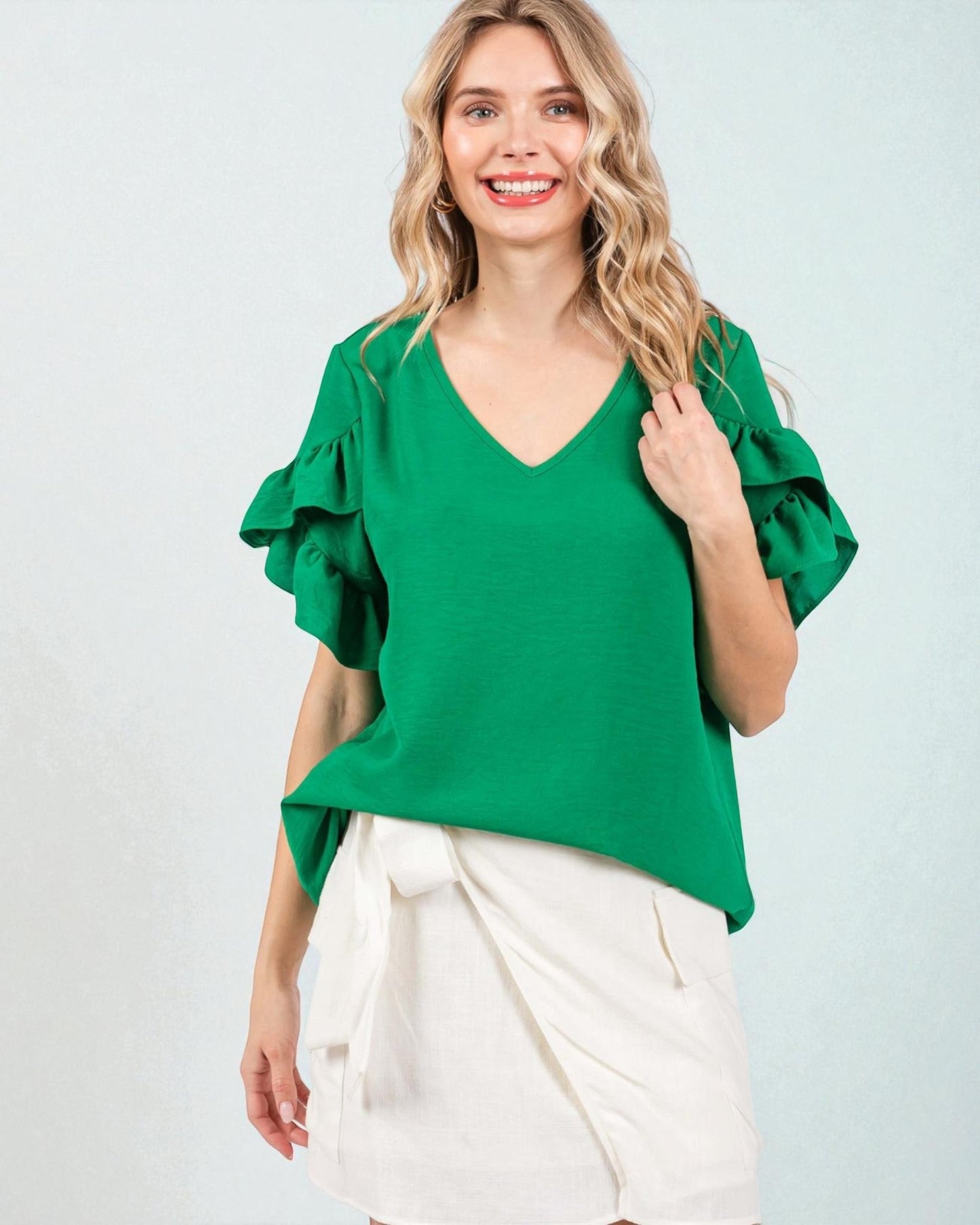 Woman wearing a green blouse with ruffled sleeves on a light gray background