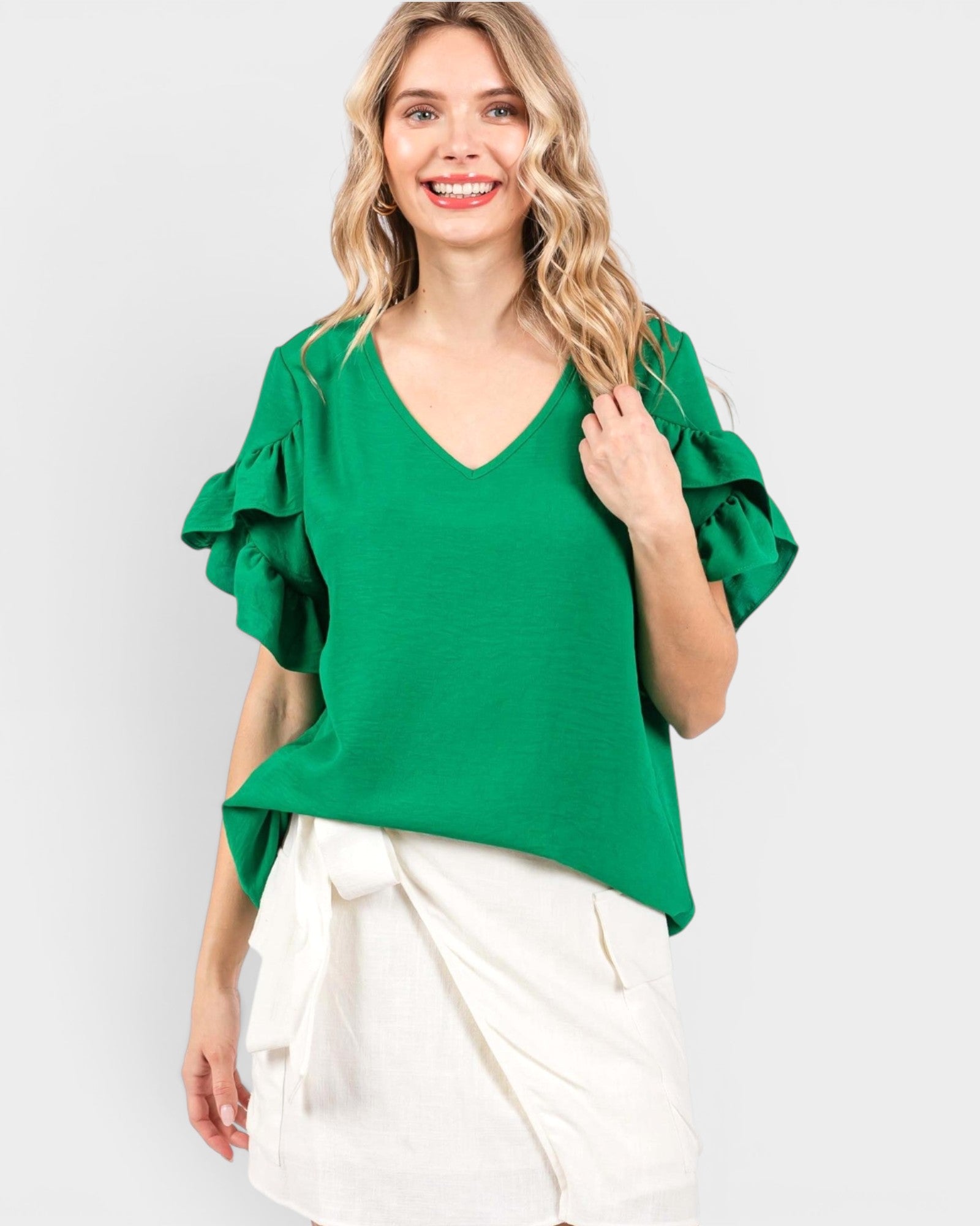 Woman wearing a green blouse with ruffled sleeves against a white background