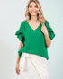 Woman wearing a green blouse with ruffled sleeves on a light gray background