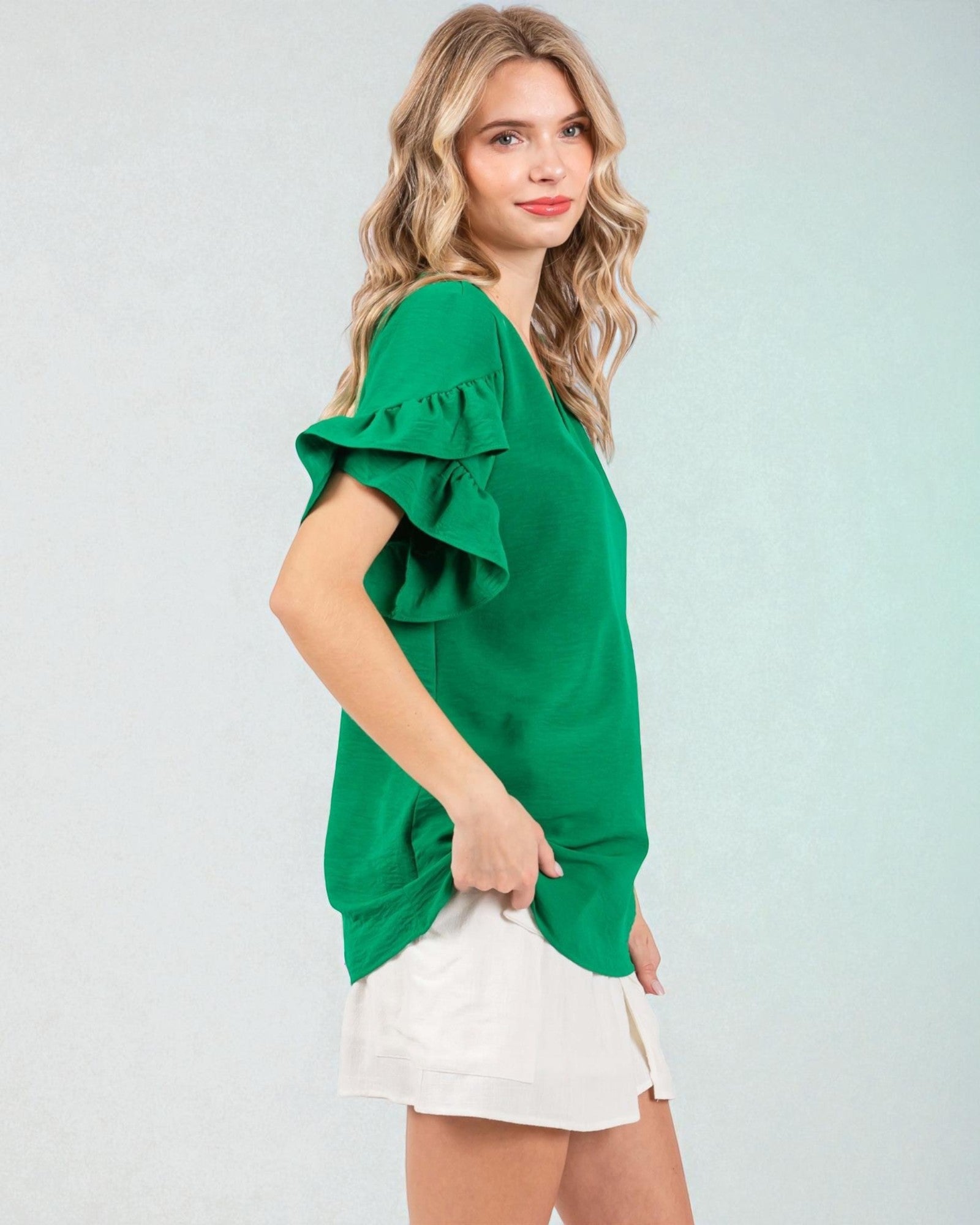 Woman wearing a green blouse with ruffled sleeves against a light gray background