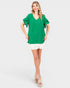 Woman wearing a green blouse with ruffled sleeves and white shorts on a white background