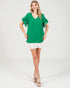 Woman wearing a green blouse with ruffled sleeves and white shorts on a white background