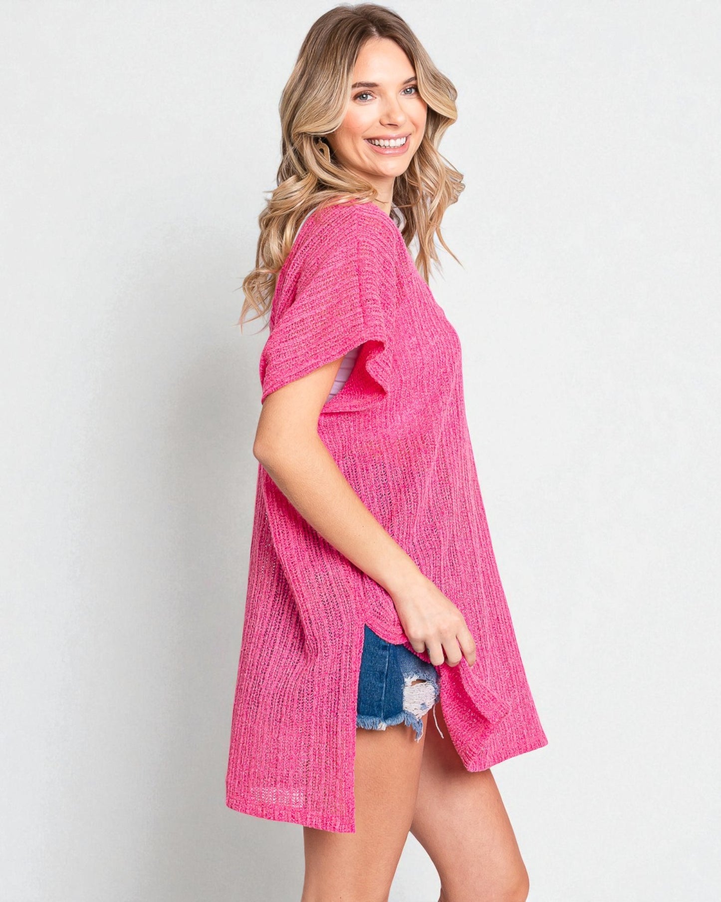 Woman wearing a pink textured dress with denim shorts on a plain background