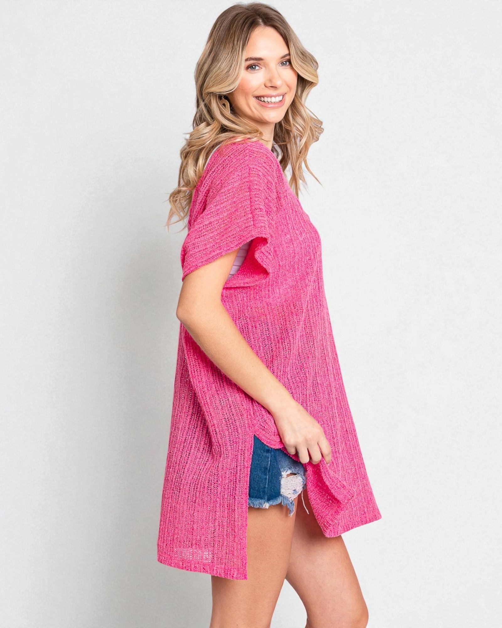 Woman wearing a pink textured dress with denim shorts on a plain background