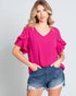 Woman wearing a bright pink blouse with ruffled sleeves and denim shorts on a gray background