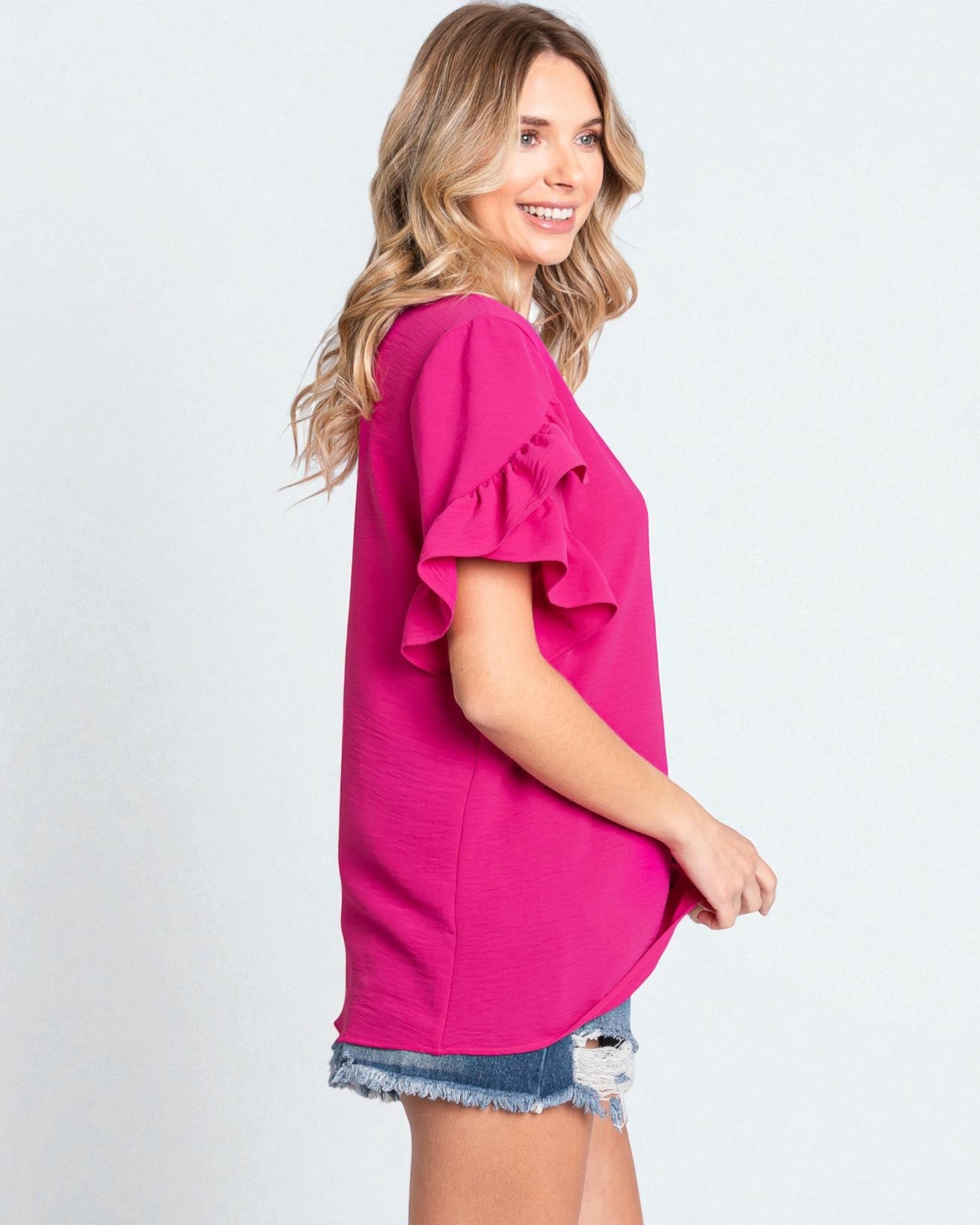 Woman wearing a bright pink blouse with ruffled sleeves on a white background