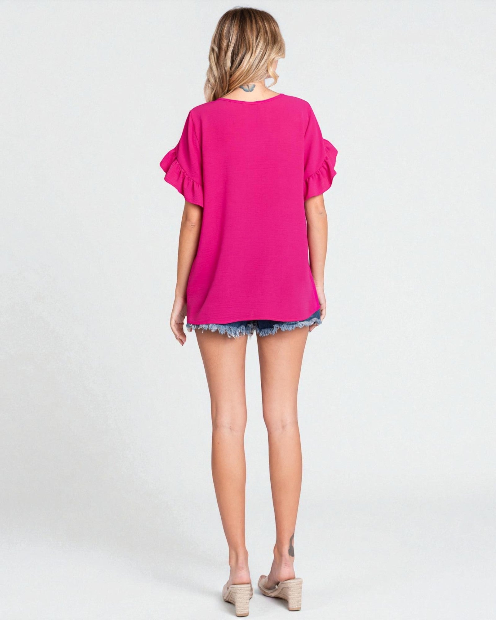 Woman wearing a bright pink top and denim shorts on a white background