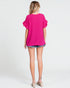 Woman wearing a bright pink top and denim shorts on a white background