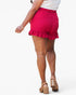 A person shown from the back wearing bright pink ruffled shorts, a white top, and tan platform sandals against a plain light gray studio background.