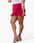 A model wearing a bright pink ruffled wrap mini skirt with a side tie, paired with tan platform sandals against a light gray studio background.
