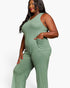 A plus-size woman wearing a sage green ribbed knit sleeveless jumpsuit with a chest pocket, shown against a plain white studio background.
