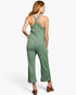 A woman shown from the back wearing a sage green ribbed jumpsuit with a crossover halter-style back and wide cropped legs, paired with brown heeled sandals against a plain light background.