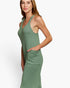 A woman modeling a sleeveless, ribbed knit halter-neck maxi dress in sage green, featuring side pockets, set against a plain white studio background.