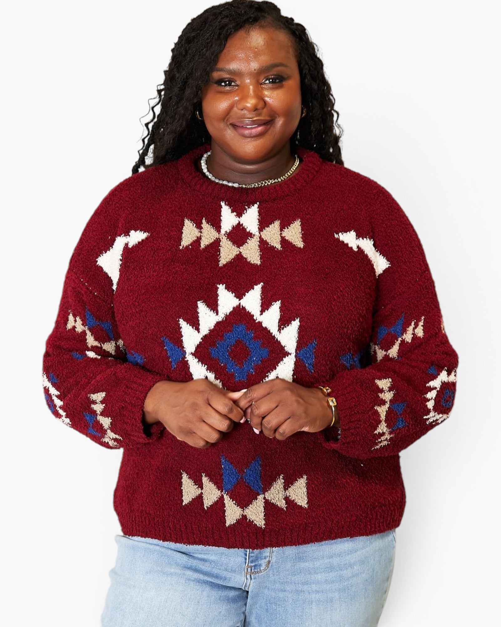 A woman wearing a fuzzy knit crewneck sweater with a Southwestern geometric pattern in burgundy, cream, and blue, paired with light blue jeans against a plain white background.