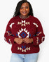 A woman wearing a fuzzy knit crewneck sweater with a Southwestern geometric pattern in burgundy, cream, and blue, paired with light blue jeans against a plain white background.