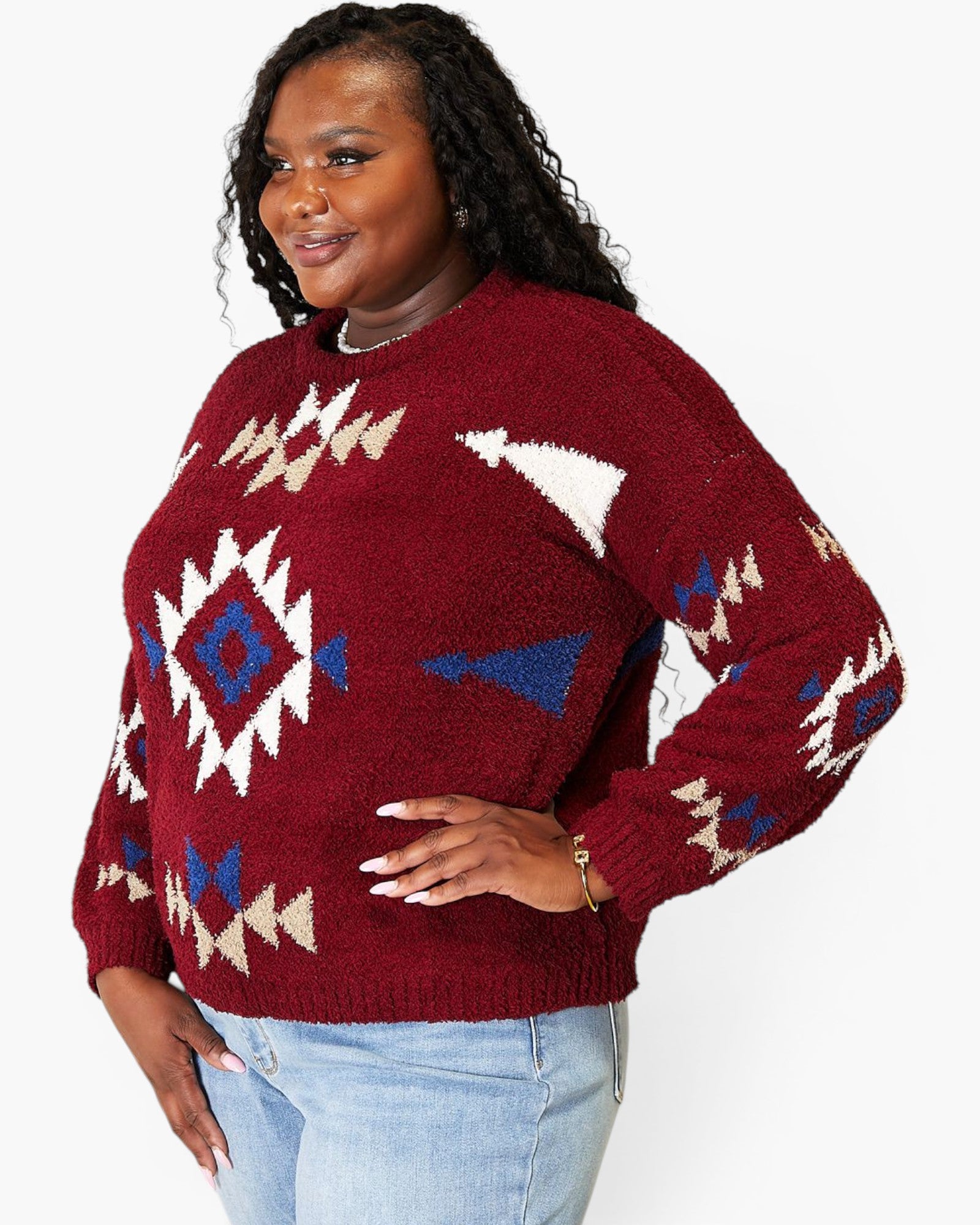 A woman wearing a fuzzy knit crewneck sweater with a Southwestern geometric pattern in burgundy, cream, and blue, paired with light blue jeans against a plain white background.