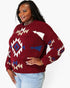 A woman wearing a fuzzy knit crewneck sweater with a Southwestern geometric pattern in burgundy, cream, and blue, paired with light blue jeans against a plain white background.