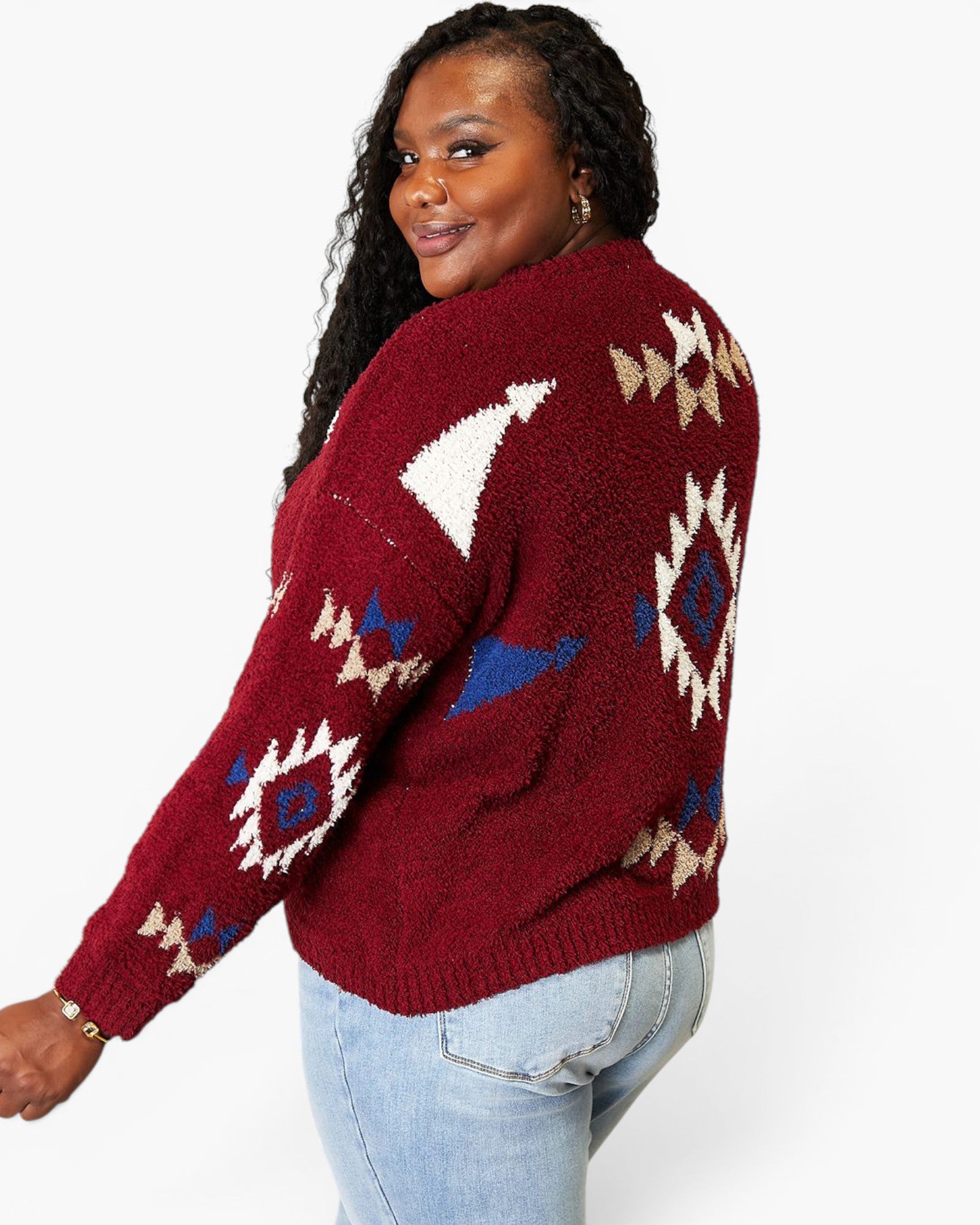 A woman wearing a maroon fuzzy knit sweater with a Southwestern geometric pattern in cream, blue, and white, paired with light-wash jeans against a plain white background.