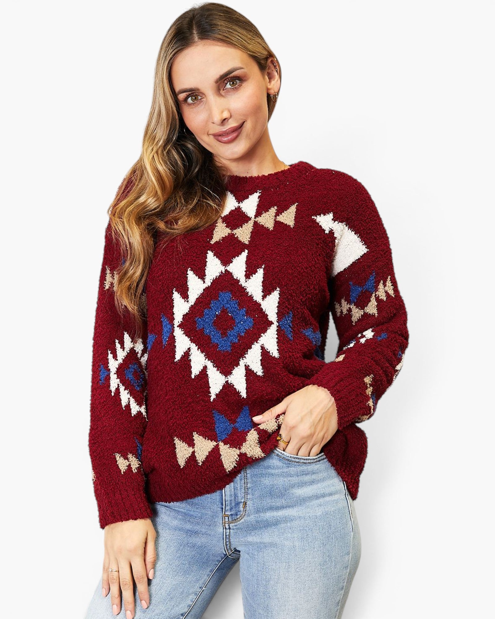 A woman wearing a maroon knit sweater with a Southwestern geometric pattern in white, beige, and blue, paired with light blue jeans, against a plain white background.