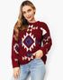 A woman wearing a maroon knit sweater with a Southwestern geometric pattern in white, beige, and blue, paired with light blue jeans, against a plain white background.