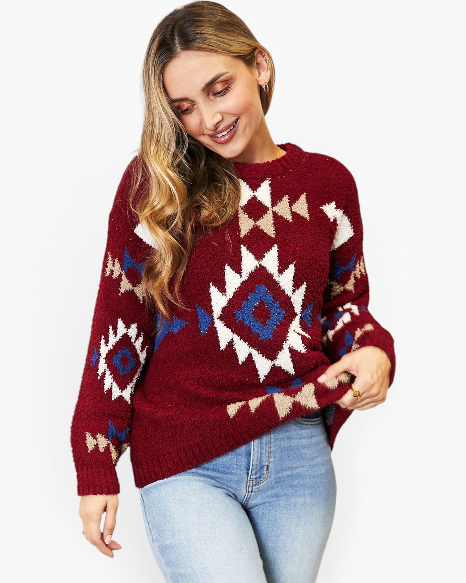 A woman wearing a long-sleeve knit sweater with a Southwestern geometric pattern in burgundy, cream, and blue, paired with light-wash jeans against a plain white background.