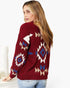 A woman wearing a fuzzy knit cardigan with a Southwestern geometric pattern in burgundy, cream, and blue, paired with light blue jeans against a white background.