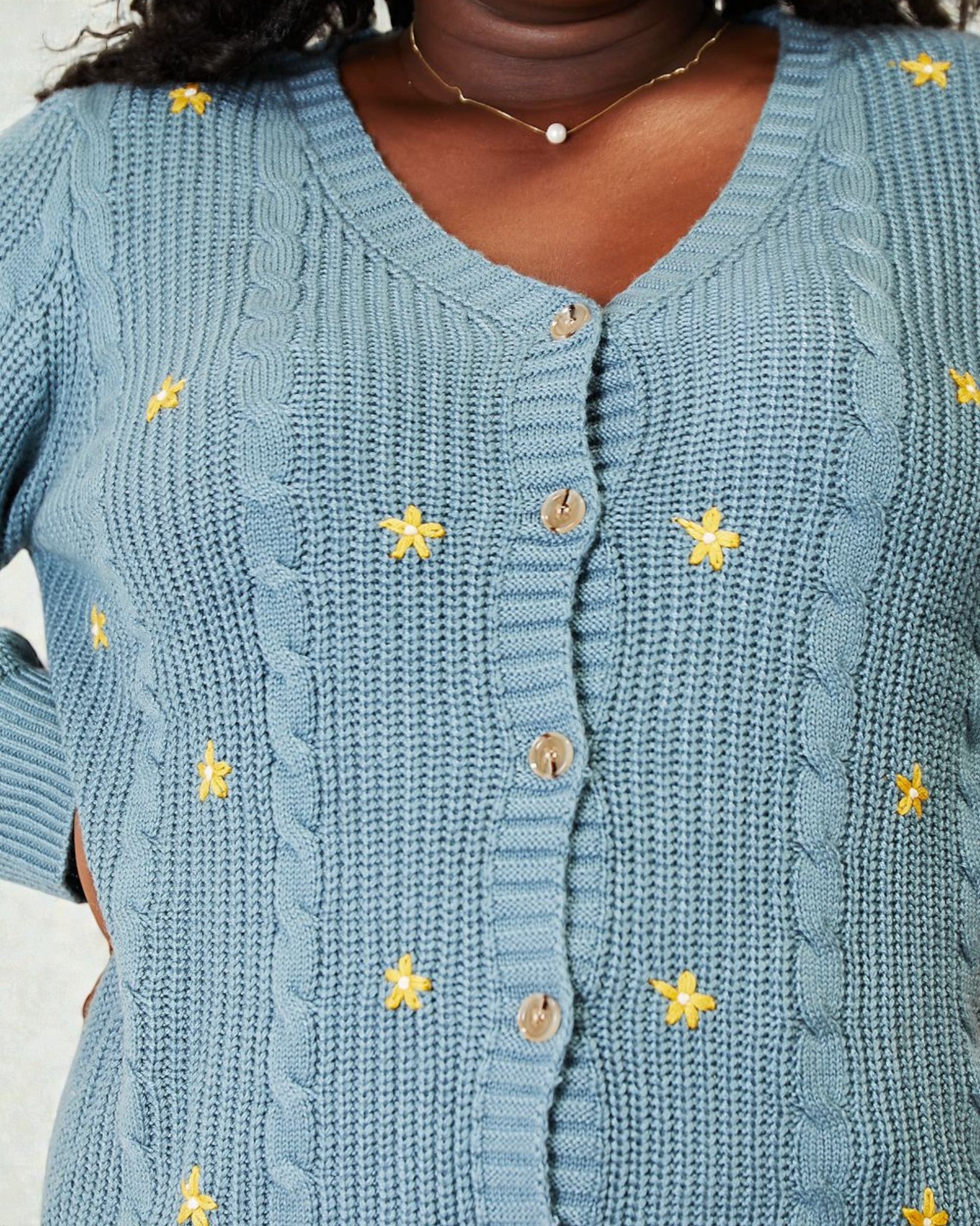 Blue knitted cardigan with yellow flower patterns on a neutral background