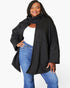 A woman modeling a black open-front cardigan with a matching draped scarf, worn over a white top and blue jeans, against a plain white background.