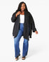 A woman modeling a black open-front cardigan over a white top and blue jeans, photographed against a plain light gray studio background.