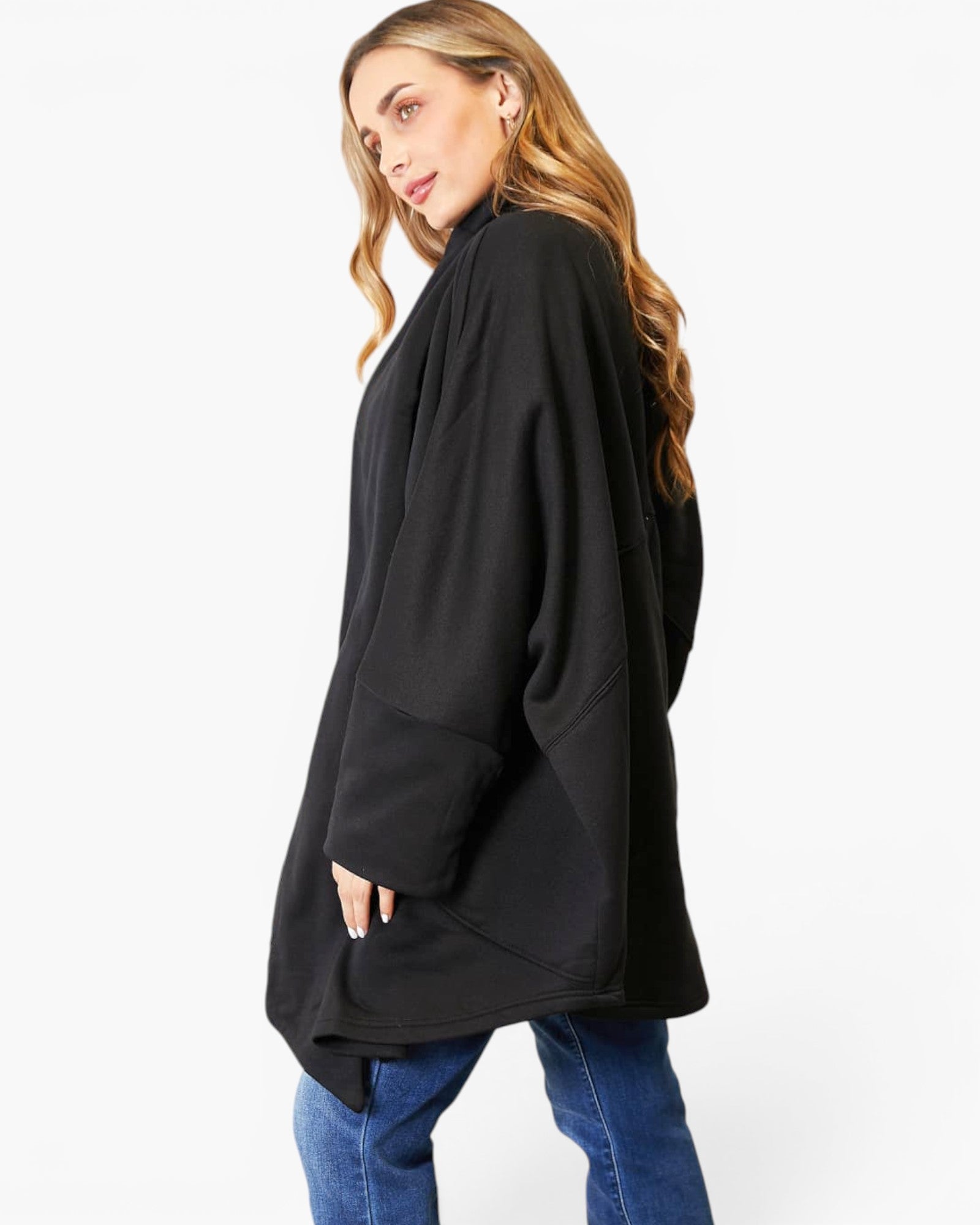 A woman wearing a black oversized turtleneck sweater with side pockets, paired with blue jeans, photographed against a plain white studio background.