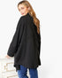 A woman wearing a loose-fitting black long-sleeve top and blue jeans, photographed from the back against a clean white studio background.