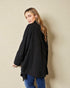 Woman wearing a black coat and blue jeans against a beige wall