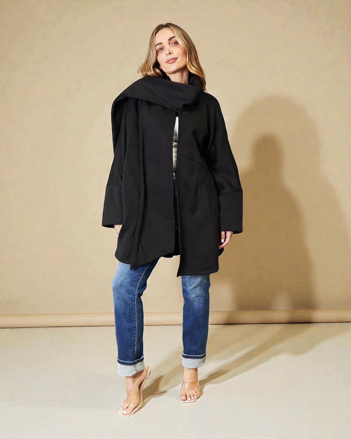 Woman wearing a black coat and blue jeans against a beige background