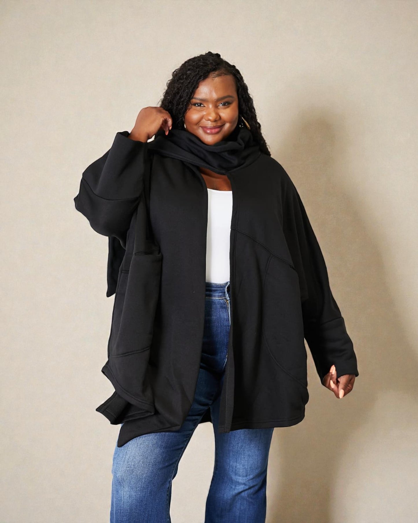 Woman wearing a black cardigan over a white top and blue jeans on a beige background