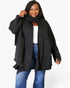 A woman modeling a black oversized open-front cardigan or jacket with a matching black scarf, worn over a white top and blue jeans, against a plain light gray studio background.