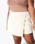 A close-up of a model wearing a light cream wrap-style mini skirt and a matching beige top against a plain white background.