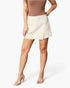 A model wearing a light beige wrap-style mini skirt with a side slit, paired with a brown top and clear high-heeled sandals, against a plain white studio background.