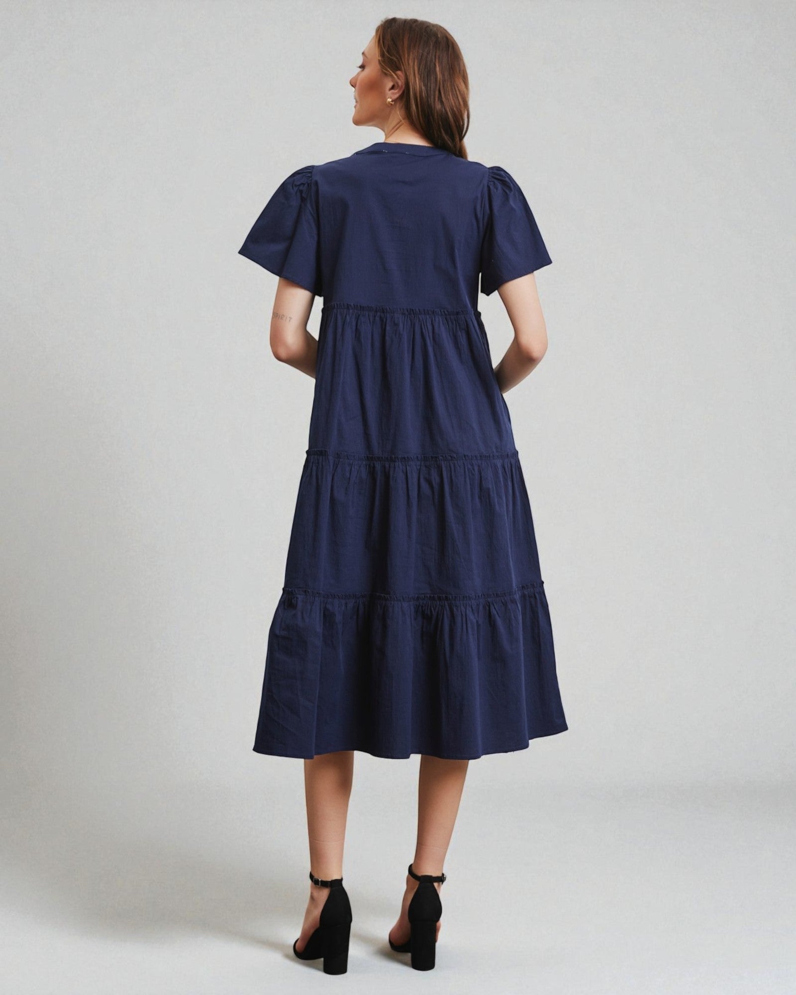 Woman wearing a navy blue dress with ruffled sleeves on a light gray background