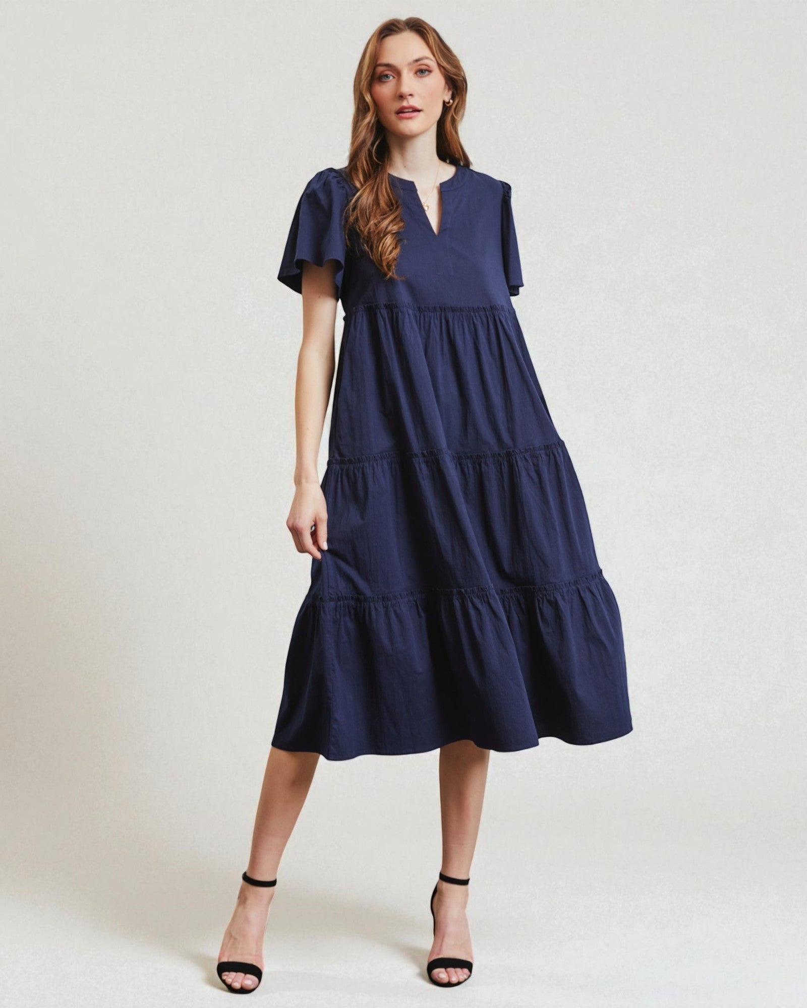 Woman wearing a navy blue dress with ruffled sleeves on a white background