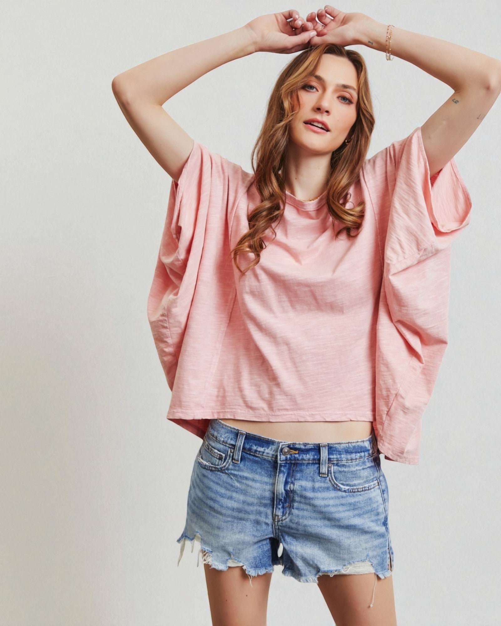 Woman wearing a pink oversized shirt and denim shorts against a plain background
