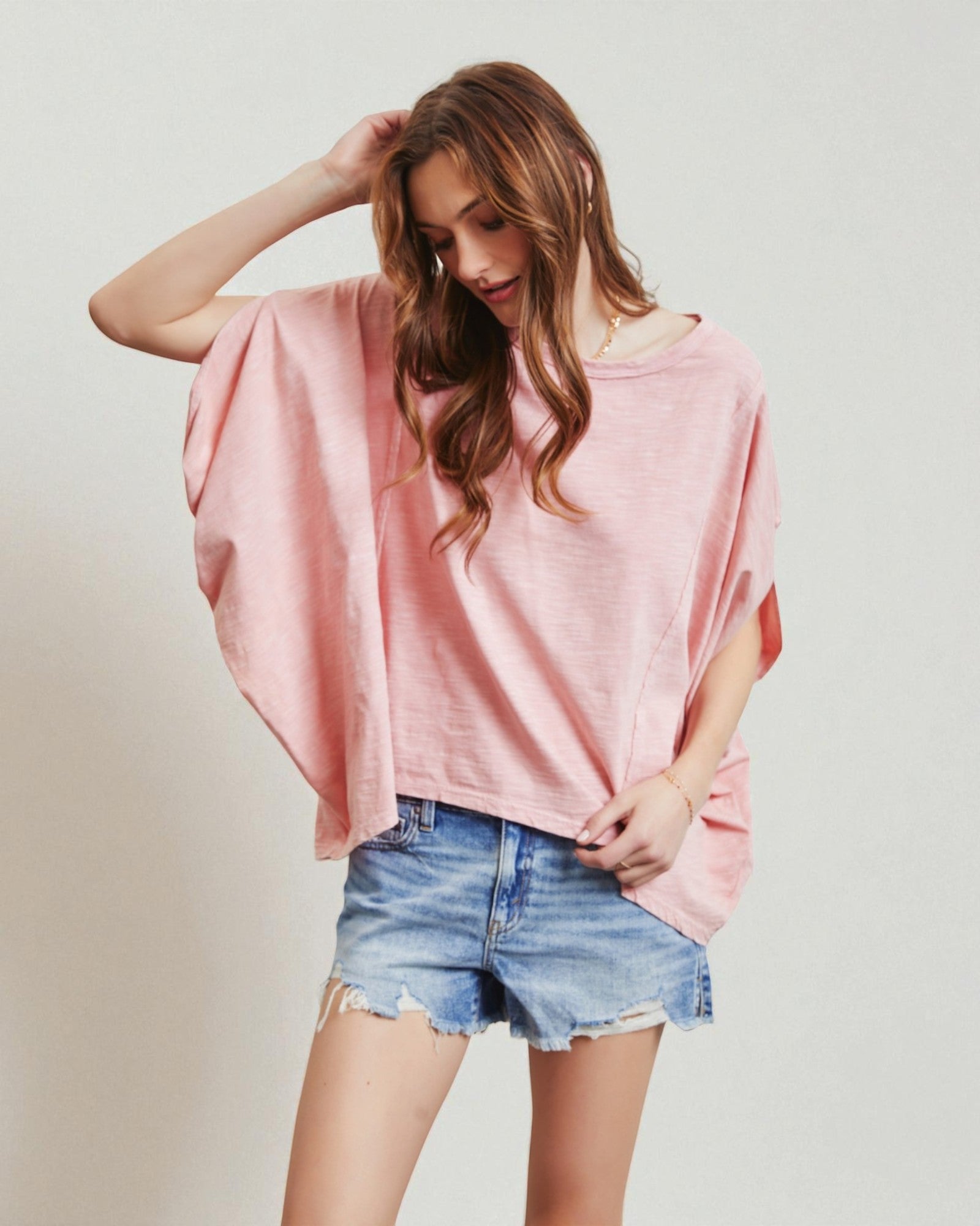 Woman wearing a pink oversized top and denim shorts on a plain background