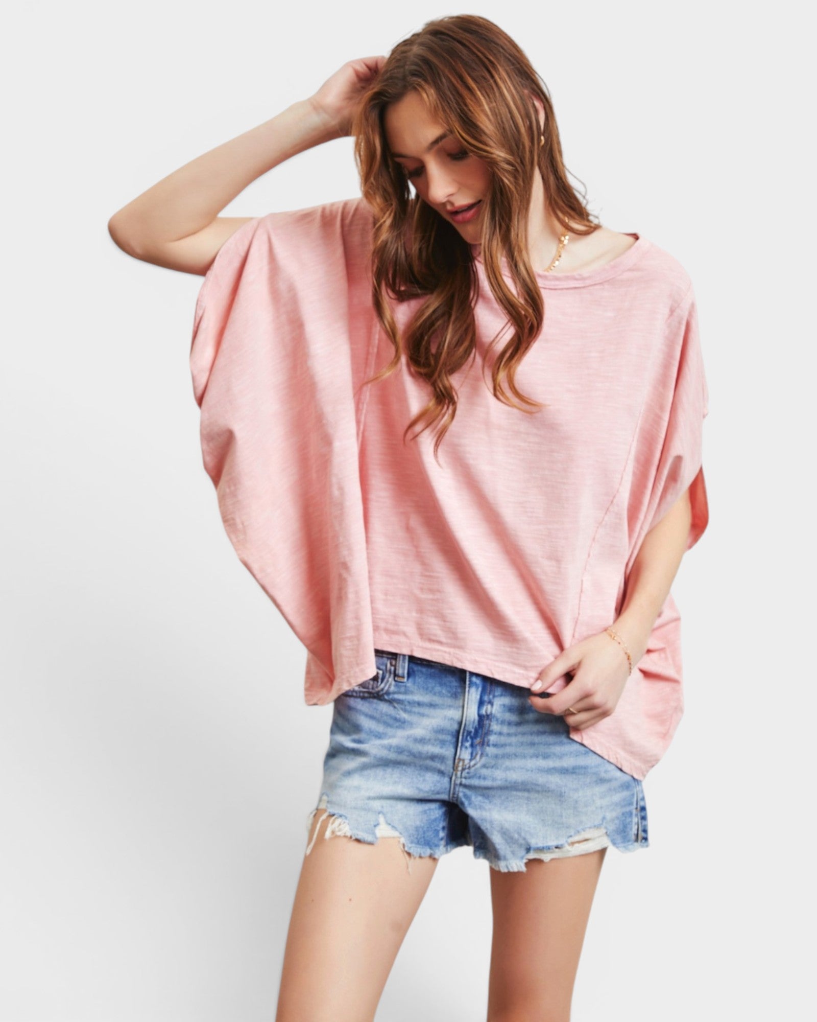 Woman wearing a pink oversized top and denim shorts on a white background